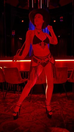Sephira, sensual muse, lit in red, dressed in lingerie standing in an empowered positon.